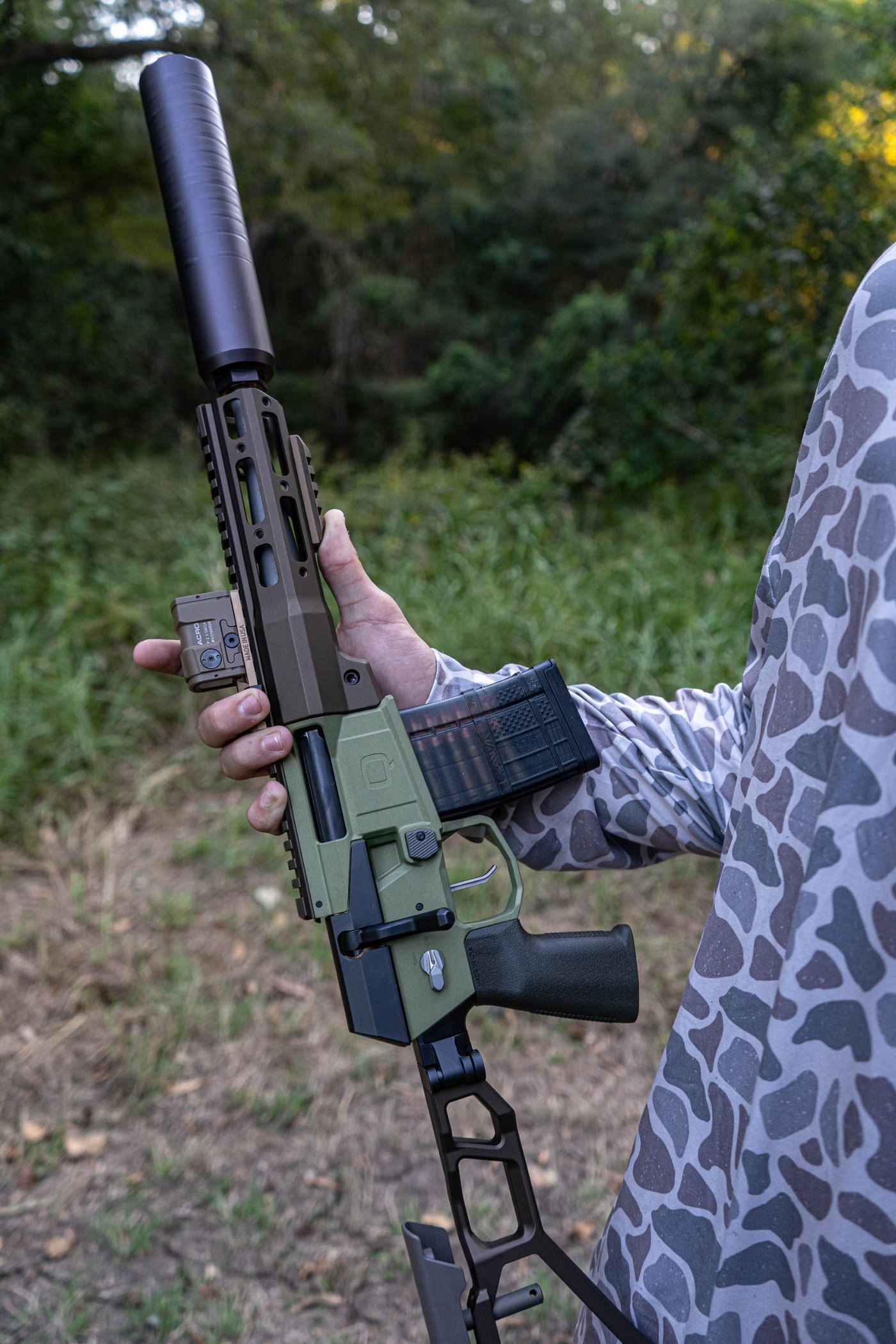 A suppressed Q Mini Fix bolt-action rifle in .300 Blackout, held in both hands in the field, trigger guard clear.